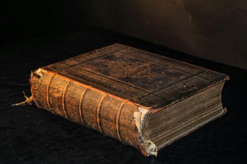 An ancient leather bound hardback with a tattered spine and cover, on black background.